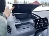 Hånd åpner oppbevaringsrom i dashbordet på Kia PV5 Cargo ved siden av infotainmentskjerm.