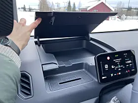 Hånd åpner oppbevaringsrom i dashbordet på Kia PV5 Cargo ved siden av infotainmentskjerm.
