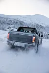 KGM Musso EV 4x4 pickup kjører på snødekt vei i fjellandskap sett bakfra.