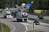 Flere lastebiler og biler kjører på en motorvei omgitt av skog.