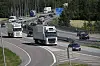 Flere lastebiler og biler kjører på en motorvei omgitt av skog.